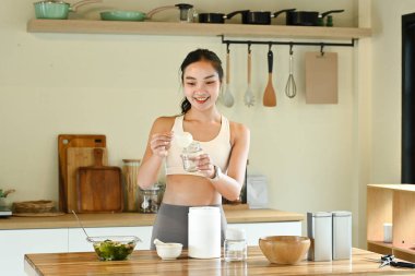 Bir kadın mutfakta, gülümsüyor ve içki hazırlıyor. Mutfak çeşitli alet edevat ve aletlerle dolu. Blender, kase, kaşık ve bardak da dahil..