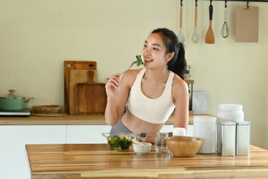 Bir kadın gülümsüyor ve önünde salatayla çatal tutuyor. Masa kâseler, fincanlar ve kaşıklarla dolu. Masanın üzerinde birkaç şişe ve kavanoz var..