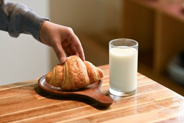 Bir insan bir bardak sütün yanında kruvasana uzanıyor. Sahne basit ve sıradan, içeceğini yudumlarken atıştırmanın tadını çıkaran kişi..