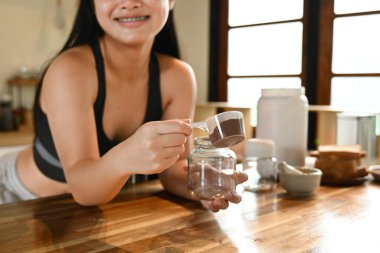 Bir kadın mutfakta protein içeceği yapıyor. Gülümsüyor ve sürecin tadını çıkarıyor..