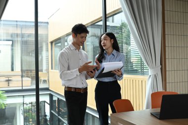 İki kişi bir dizüstü bilgisayar ve bir yığın kağıtla bir masanın önünde duruyor. Gazetelere bakıyorlar ve bir şey tartışıyorlar..