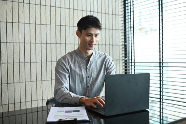 Önünde dizüstü bilgisayarı olan bir adam masada oturuyor. Gülümsüyor ve işinden zevk alıyor..
