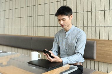 Adamın biri elinde dizüstü bilgisayar ve cep telefonu olan bir masada oturuyor. Elinde bir fincan tutarken cep telefonuna bakıyor. Sahne, adamın çalışıyor ya da telefonunda interneti karıştırıyor olabileceğini gösteriyor..