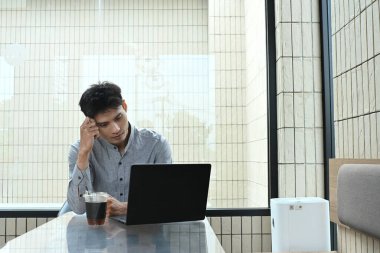 Önünde dizüstü bilgisayarı olan bir adam masada oturuyor. Ekrana bakıyor ve derin düşüncelere dalmış...