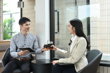 İki kişi bir masada oturuyor, biri bir fincan kahve tutuyor. Gülümsüyorlar ve birbirlerinin arkadaşlığından zevk alıyor gibiler..