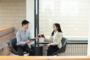 İki kişi bir masada oturuyor, biri bir fincan kahve tutuyor. Gülümsüyorlar ve birbirlerinin arkadaşlığından zevk alıyor gibiler.