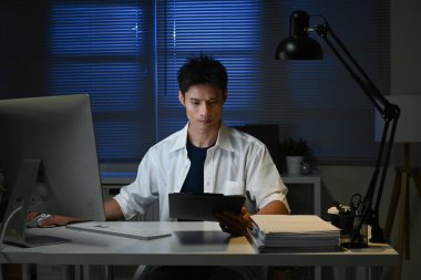 İş yerinde genç bir işadamının gece geç saatlerde dijital tablet kullanması...