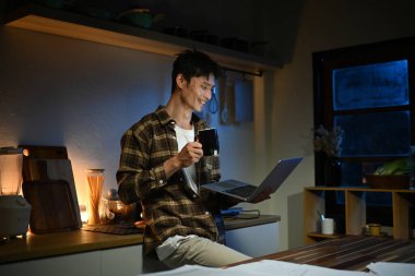 Genç adam oturur bardaki mutfakta sayaç içinde laptop çalışır ve bir kahve içiyor. Ev atmosferi, akşam zor bir gün sonra adet eser bulunmaktadır. Ev ofis..