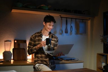 Genç adam oturur bardaki mutfakta sayaç içinde laptop çalışır ve bir kahve içiyor. Ev atmosferi, akşam zor bir gün sonra adet eser bulunmaktadır. Ev ofis..