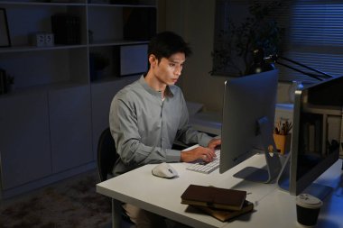 İşi bitirmek için geç saatlere kadar kalıyorum. Genç bir iş adamının geç saatlere kadar masasında bilgisayar kullanırken görüntüsü...