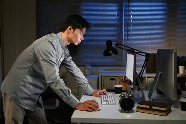 Bir adam gece elinde bir bilgisayar ve klavyeyle bir masada duruyor. Bilgisayar ekranına bakıyor.