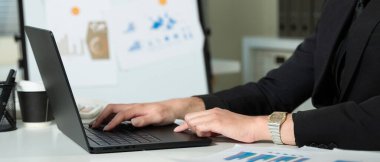 Takım elbiseli bir adam dizüstü bilgisayar tutuyor. Siyah bir kravat takıyor ve dizüstü bilgisayarda yazıyor...