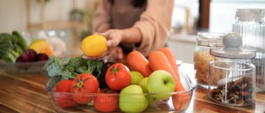 Meyve ve sebze dolu bir masanın önünde duran bir kadın elinde bir limon tutuyor.