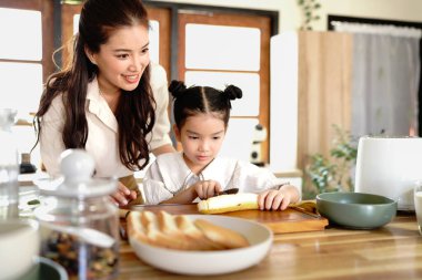 Sevecen, tatlı ilkokul kızı, şefkatli annesinin sağlıklı bir kahvaltı hazırlamasına, tahtada taze meyve dilimlemesine, mutfakta yemek yaparken iletişim kurmasına ve paylaşmasına yardım ediyor..