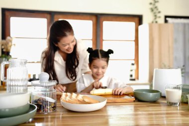 Sevecen, tatlı ilkokul kızı, şefkatli annesinin sağlıklı bir kahvaltı hazırlamasına, tahtada taze meyve dilimlemesine, mutfakta yemek yaparken iletişim kurmasına ve paylaşmasına yardım ediyor..