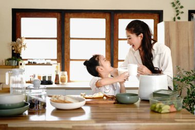Elinde kahve tutan bir anne ve süt içen genç bir kız. Kadın gülümsüyor ve kız bir fincandan su içiyor. Sahne yemek masası ve yemekle bir mutfakta geçiyor...