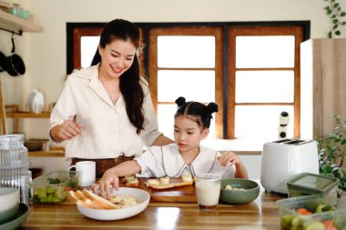 Bir anne ve bir çocuk mutfakta yemek hazırlıyorlar. Kadın gülümsüyor. Mutfak çeşitli alet ve gereçlerle dolu..