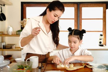 Bir anne ve bir çocuk mutfakta yemek hazırlıyorlar. Kadın gülümsüyor. Mutfak çeşitli alet ve gereçlerle dolu..