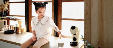 Genç bir kız pencerenin yanındaki mutfak tezgahında oturuyor ve ekmek yiyor. Mutfak çeşitli aletler ve aletlerle donatılmıştır..