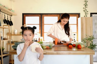 Küçük bir kız beklerken bir anne sebze kesiyor. Kız mutfakta ekmek yiyor...