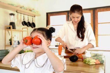 Bir anne, gözünün içinde domates tutan bir çocuğun sırtını kesiyor. Sahne neşeli ve neşeli, kadın ve çocuk birlikte mutfaktan keyif alıyorlar.