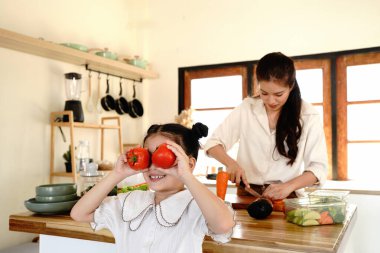 Bir anne, gözünün içinde domates tutan bir çocuğun sırtını kesiyor. Sahne neşeli ve neşeli, kadın ve çocuk birlikte mutfaktan keyif alıyorlar..
