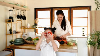 Bir anne, gözünün içinde domates tutan bir çocuğun sırtını kesiyor. Sahne neşeli ve neşeli, kadın ve çocuk birlikte mutfaktan keyif alıyorlar..