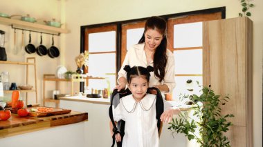 Anne, kızının okula hazırlanmasına yardım ediyor, sırt çantası ve kitaplarla ona yardım ediyor, mutfakta sandviç yapıyor, sarılıyor ve evi terk ediyor..