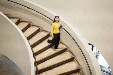 A girl walking up a spiral staircase with a book in her hand. Concept of curiosity and exploration, as the girl is likely heading to a new destination or seeking knowledge.