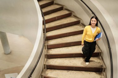 A girl walking up a spiral staircase with a book in her hand. Concept of curiosity and exploration, as the girl is likely heading to a new destination or seeking knowledge