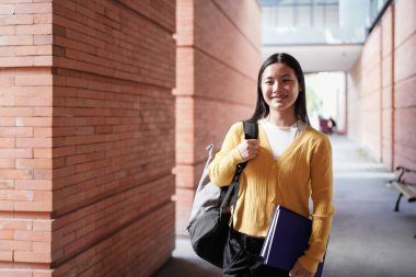 Sırt çantası ve planlayıcısı okul kampüsünde duran gülümseyen lise öğrencisinin portresi..