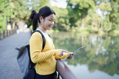 beautiful Asian girl student holding tablet and smiling at camera and learning and education concept on park in summer for relax time.