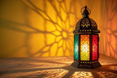 Çok güzel işlenmiş bir Fas feneri. Karmaşık metal işçiliği ve kırmızı, yeşil ve sarı tonlarda renkli vitray panellerle süslenmiş. Sıcak, davetkar bir parıltı yayıyor. Fener açık renkli bir yüzeyde duruyor. Süslü gölge desenleri Danci.