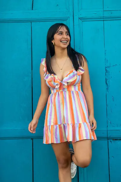 beautiful young latina smiling in a colorful dress. In the background an old colonial wooden door painted blue.