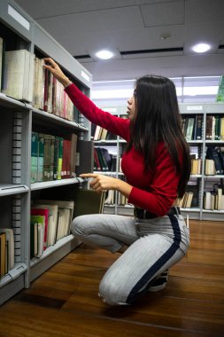 Okul kütüphanesindeki kitaplıkta kitap arayan genç bir kız. Okula geri dön.