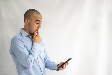 Cep telefonu ekranına bakan etkileyici ve şok olmuş kel bir adam.