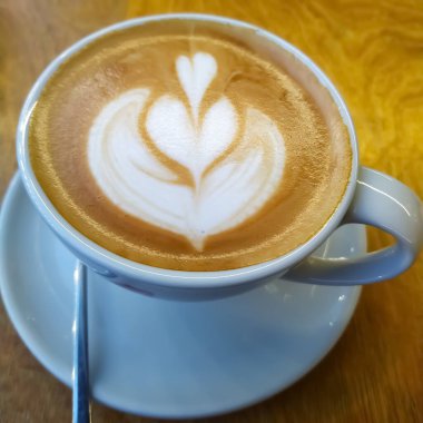 Sabah ayini için ahşap bir masanın üzerinde latte desenli bir fincan aromalı kahvenin yakın çekimi..