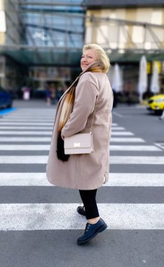 Güzel, mutlu, ceketli yaşlı bir kadın alışveriş merkezine gidiyor ve onunla birlikte arıyor. Yumuşak arkaplan ayrışması.