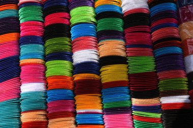 Değişik renklerde geleneksel bileziklerin canlı ve simetrik deseni, düzenli bir şekilde sıralanmış. Çoğunlukla cam, metal veya plastikten yapılmış bu dekoratif bilezikler, özellikle Hindistan ve Bangladeş 'te, Güney Asya kültürlerinde popülerdir..