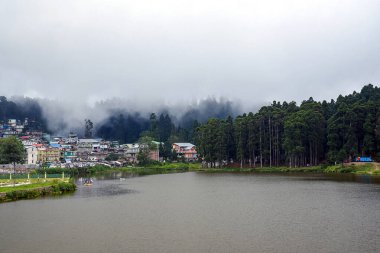 Huzurlu bir göl manzarası sergileniyor. Uzun ağaçların arasına yerleşmiş büyüleyici bir köy. Sabah sisiyle kaplanmış. Yumuşak bulutlar havada süzülerek, Batı Bengal 'in Mirik kentindeki bu huzurlu ve sakin doğal manzaranın atmosferini güçlendirir.