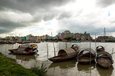 Birkaç geleneksel ahşap tekne, bulutlu bir öğleden sonra gökyüzünün altındaki şehir binalarının arka planına karşı, huzurlu bir şekilde demirlemiştir. Bu sahne, doğal deniz kıyısındaki yaşamla şehir mimarisini güzel bir şekilde harmanlıyor..