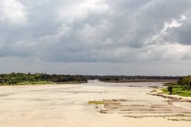 Dolambaçlı bir nehir sessiz bir kırsal alanda, yemyeşil ağaçlar ve açık araziler tarafından çevrelenmiş bir şekilde yavaşça dolaşır..