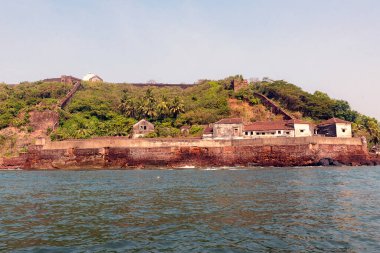 Yüzyıllar öncesinden kalma eski bir kıyı kalesi Hindistan, Goa 'da yemyeşil ve yıpranmış taş duvarlarla çevrili bir yamaçta gururla duruyor. Gün ortası güneşiyle yıkanmış ve denize bakan.