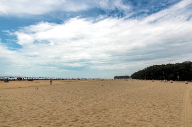 Ziyaretçiler rahatlar ve parçalı bulutlu bir gökyüzünün altında Coxs Bazar, Bangladeş 'teki geniş kumlu plajda oynarlar..