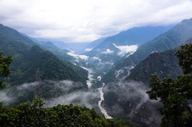 Kuzey Sikkim, Hindistan 'daki Mangan Manzara Noktası' ndan nefes kesici bir manzara, Doğu Himalayalar 'ın panoramik manzaralarını sunuyor. Manzarada yuvarlanan yeşil tepeler, sis kaplı dağ sıraları ve uzak karlı zirveler yer alıyor..
