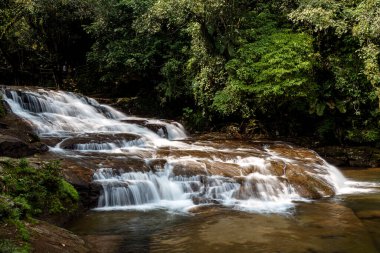 İsimsiz bir şelale, Hindistan 'ın Meghalaya kentindeki Mawlynnong kentindeki ünlü canlı kök köprüsünün yanında yavaşça akar. Yoğun orman ve doğal kaya oluşumlarıyla çevrelenen şelale, bu eko-turizm beldesinin dingin cazibesini artırıyor..