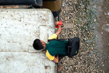 Genç bir adam bir trenin tepesinde dengesiz bir şekilde kırmızı bir nesneyi tutarken görülüyor. Bu şehir manzarası, canlı bir şehirde gündüz saatlerinde günlük hayatın hareketlerini yakalar..