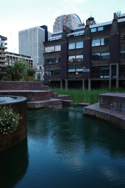 Arkasında saat kulesi olan bir binanın önünde bir gölet.