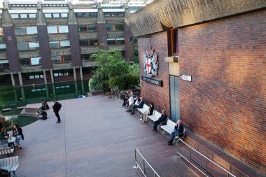 Bir grup insan avludaki banklarda oturuyor.