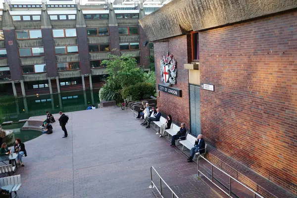 Bir grup insan avludaki banklarda oturuyor.